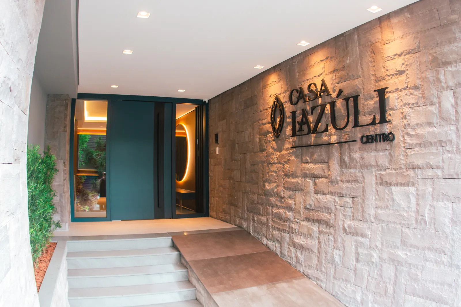 Entrada da Casa Lazúli, com o logo na parede de pedra